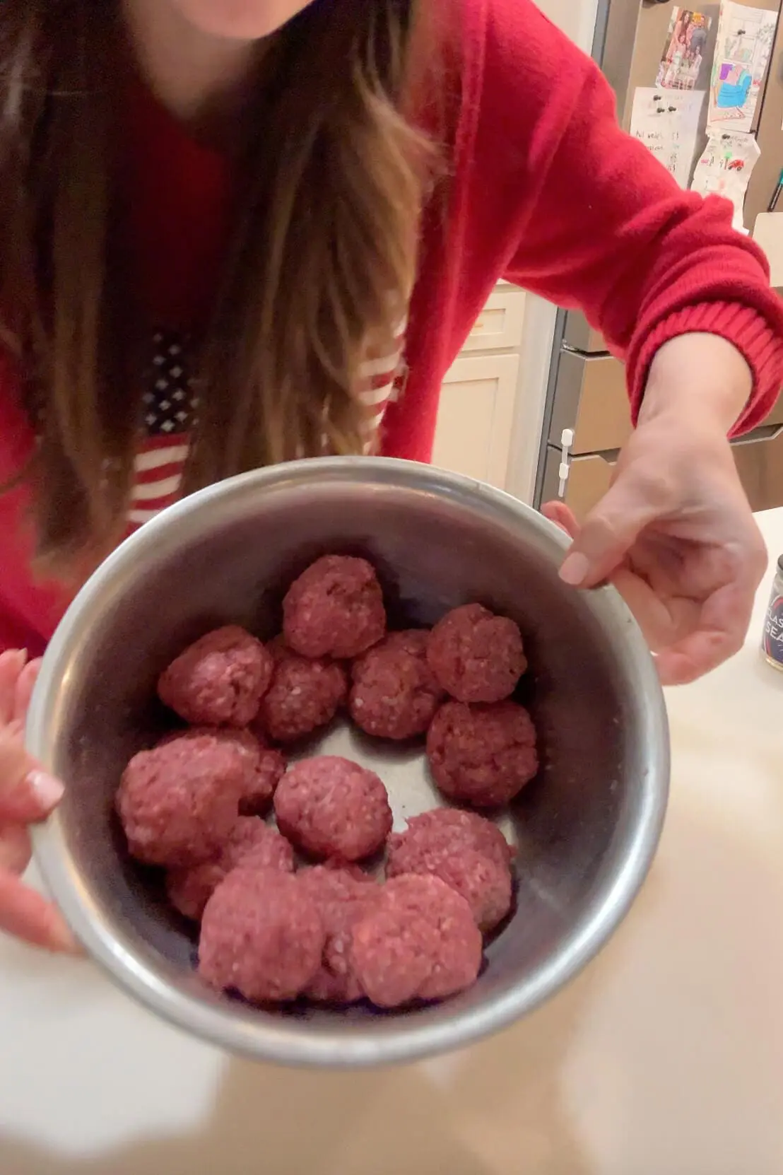 The woman holds up a metal bowl filled with raw, hand-formed burger patties, showing them off before they hit the griddle.